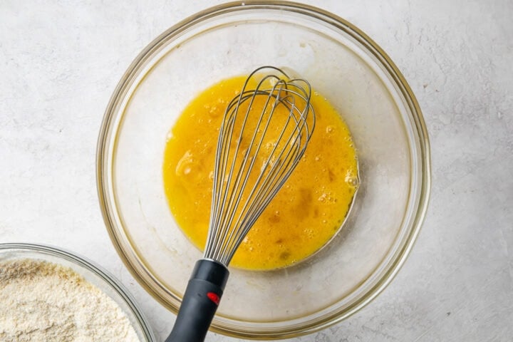 Wet ingredients for paleo pancakes in a large glass mixing bowl with a whisk.