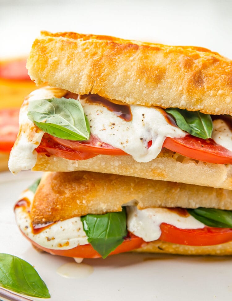 Two halves of a caprese sandwich stacked on top of each other, showing the melted cheese and bright red tomato.