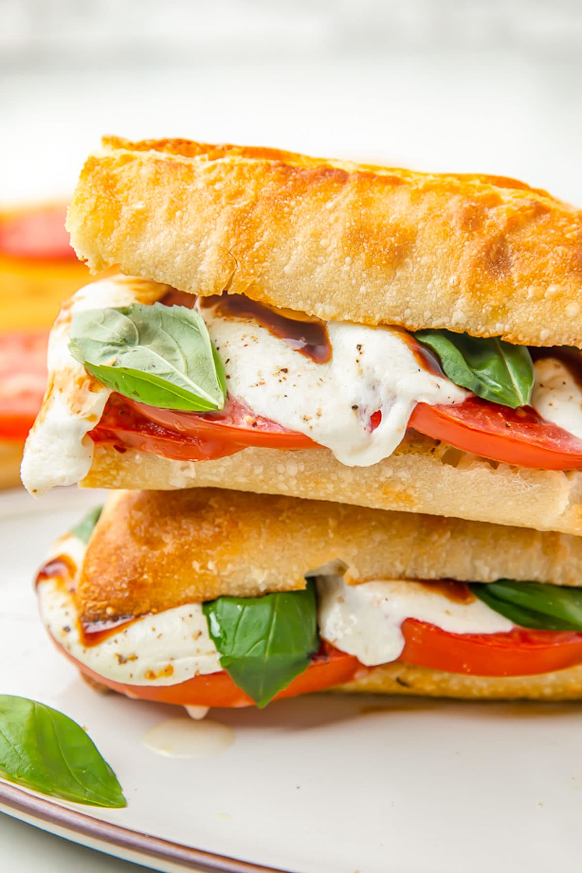 Two halves of a caprese sandwich stacked on top of each other, showing the melted cheese and bright red tomato.
