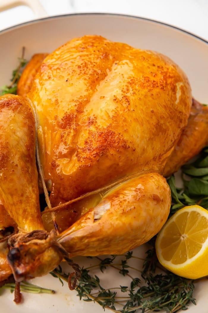 Close-up of a whole chicken on a bed of herbs with half a lemon