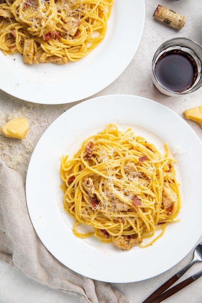 Two plates of chicken carbonara with a glass of red wine