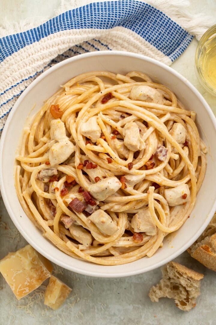 A large white bowl of creamy chicken carbonara on a table with a blue and white kitchen towel.