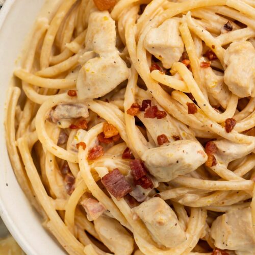 Close-up of a large white bowl of creamy chicken carbonara on a table with a blue and white kitchen towel.