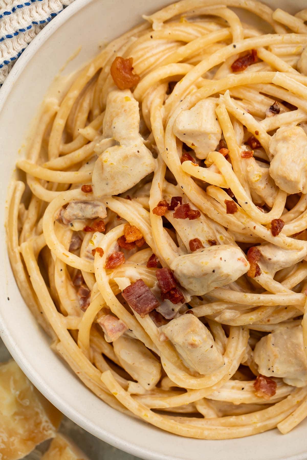 Close-up of a large white bowl of creamy chicken carbonara on a table with a blue and white kitchen towel.