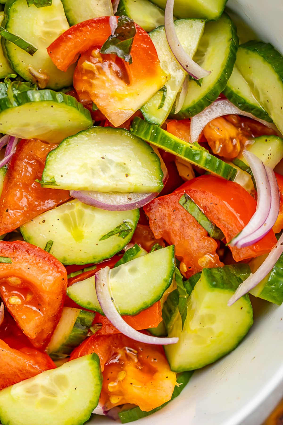 Close-up of a bowl holding a cucumber tomato salad with slices of red onion and an easy vinaigrette.