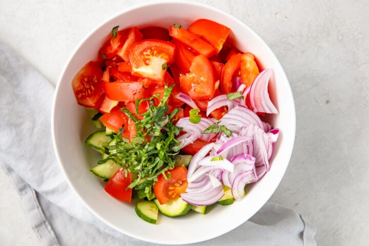 Ingredients for cucumber tomato salad in a large white bowl.