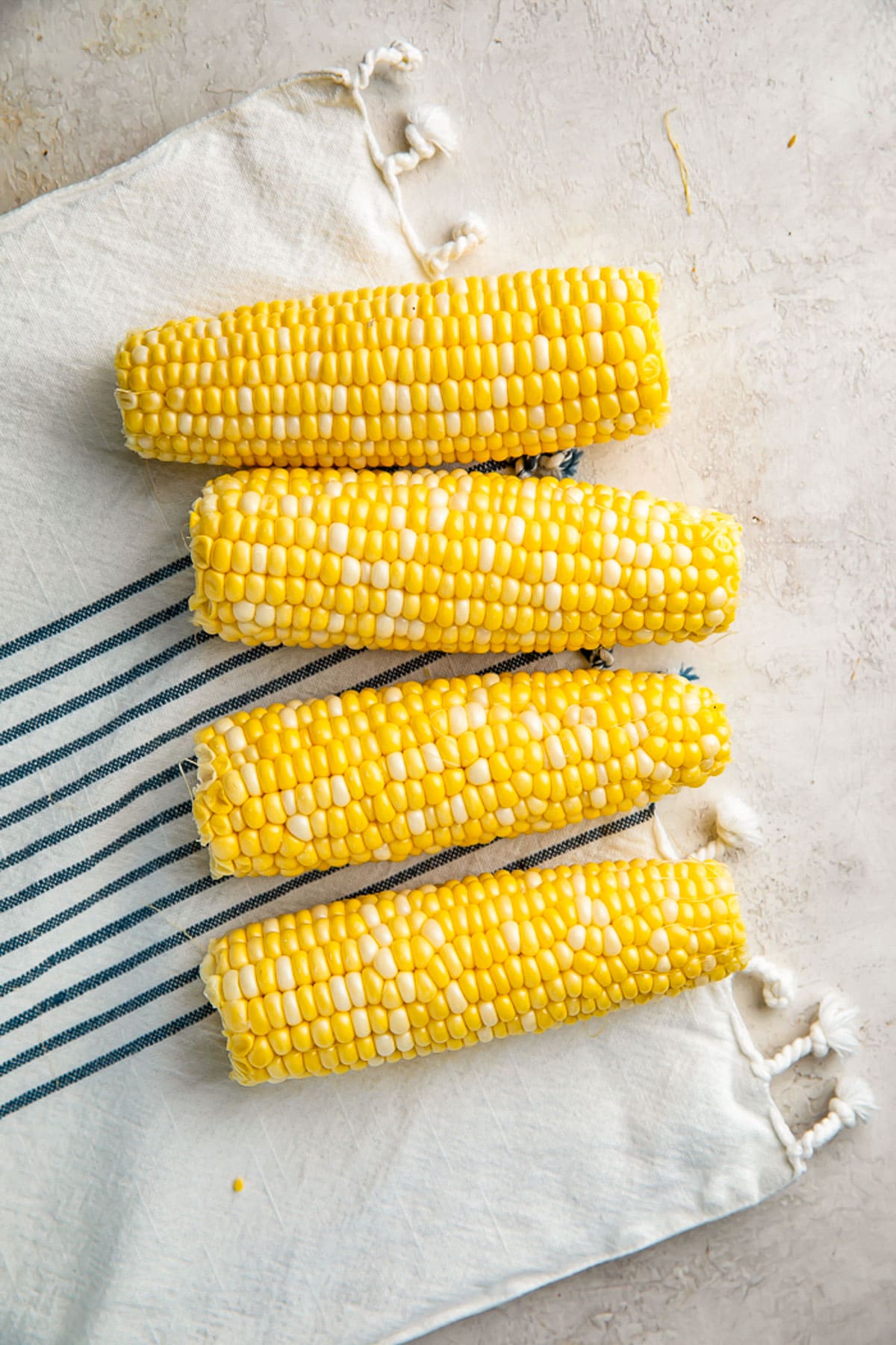 4 ears of raw, shucked corn on the cob on a neutral table with a cloth napkin.