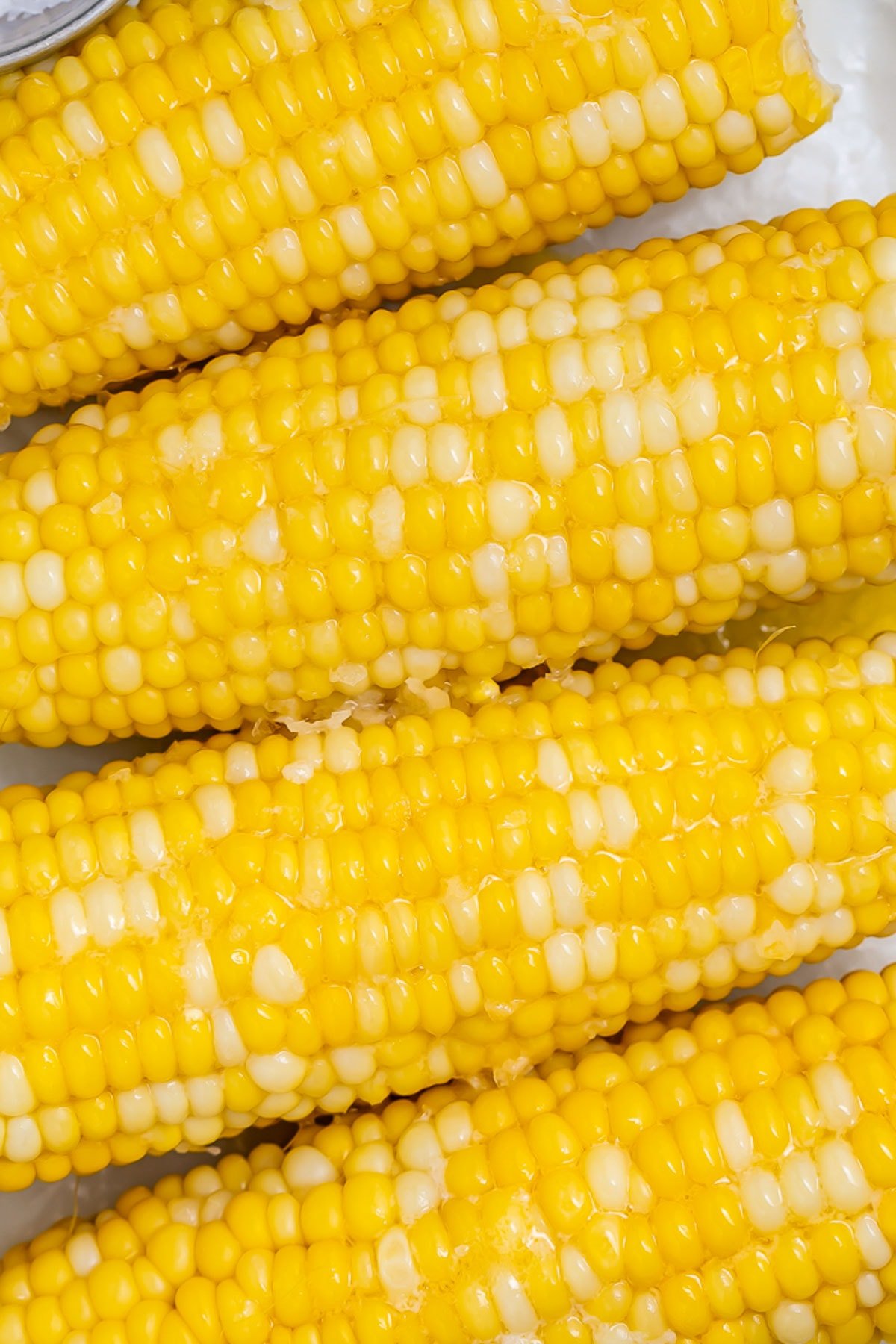 Close-up of 4 ears of boiled corn on the cob topped with melty butter.