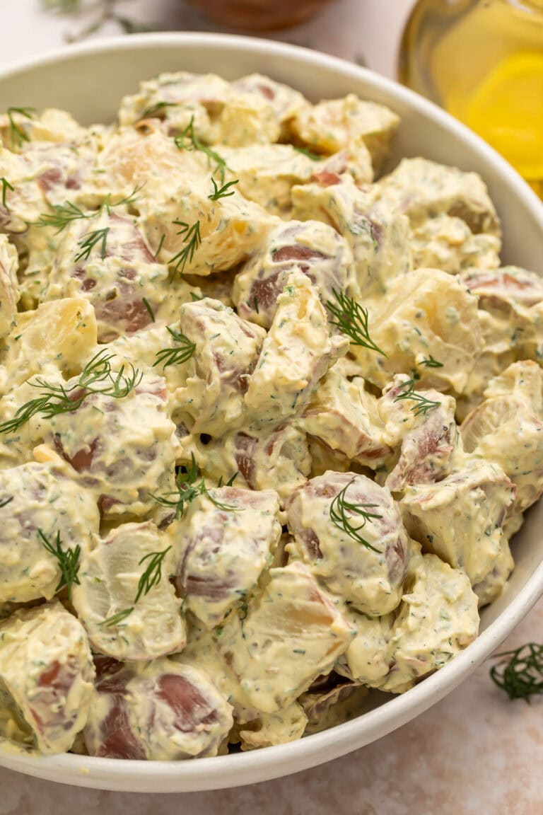 A large white bowl of creamy red potato salad with fresh herbs.