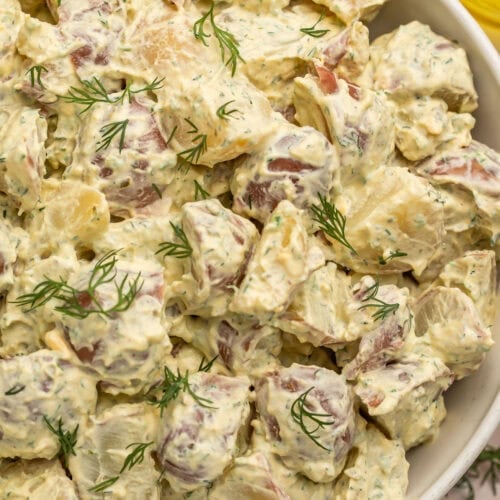 A large white bowl of creamy red potato salad with fresh herbs.