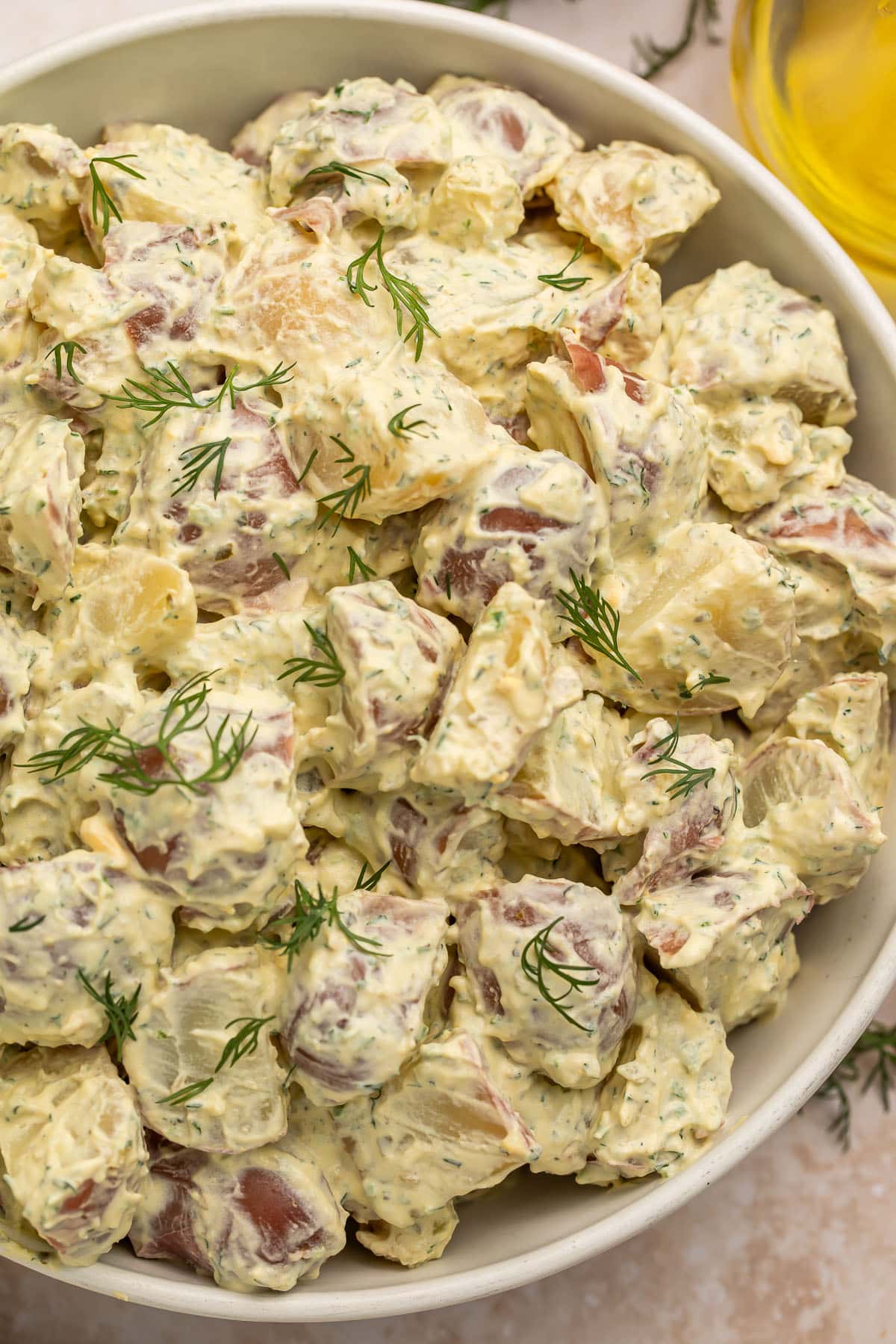 A large white bowl of creamy red potato salad with fresh herbs.