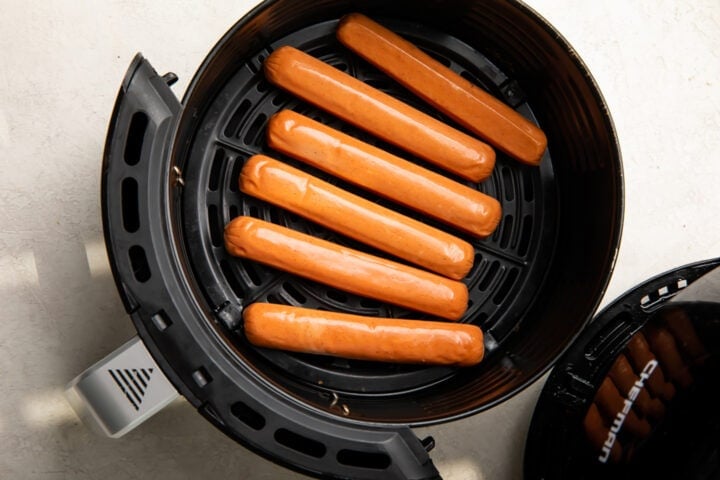 Uncooked hot dogs in an air fryer basket.
