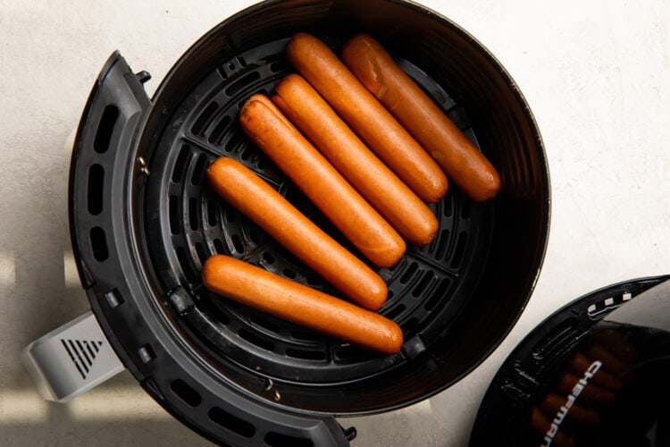 Cooked hot dogs in an air fryer basket.