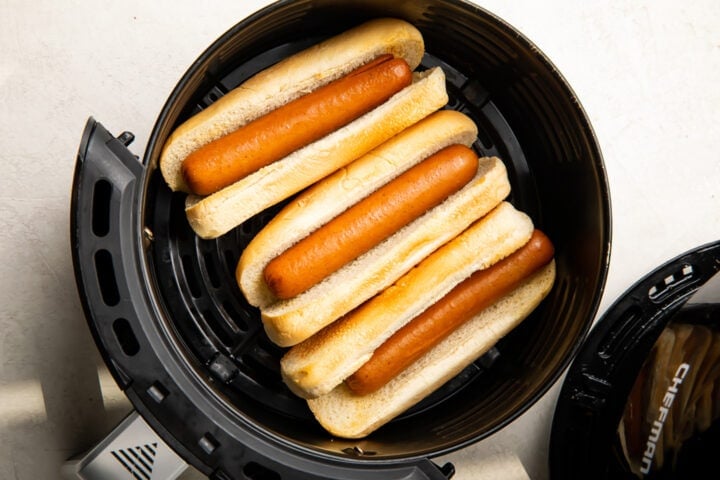 Hot dogs in hot dog buns in an air fryer basket.