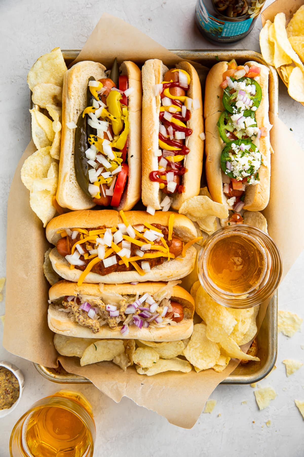 5 air fryer hot dogs in hot dog buns with various toppings arranged on a baking sheet.