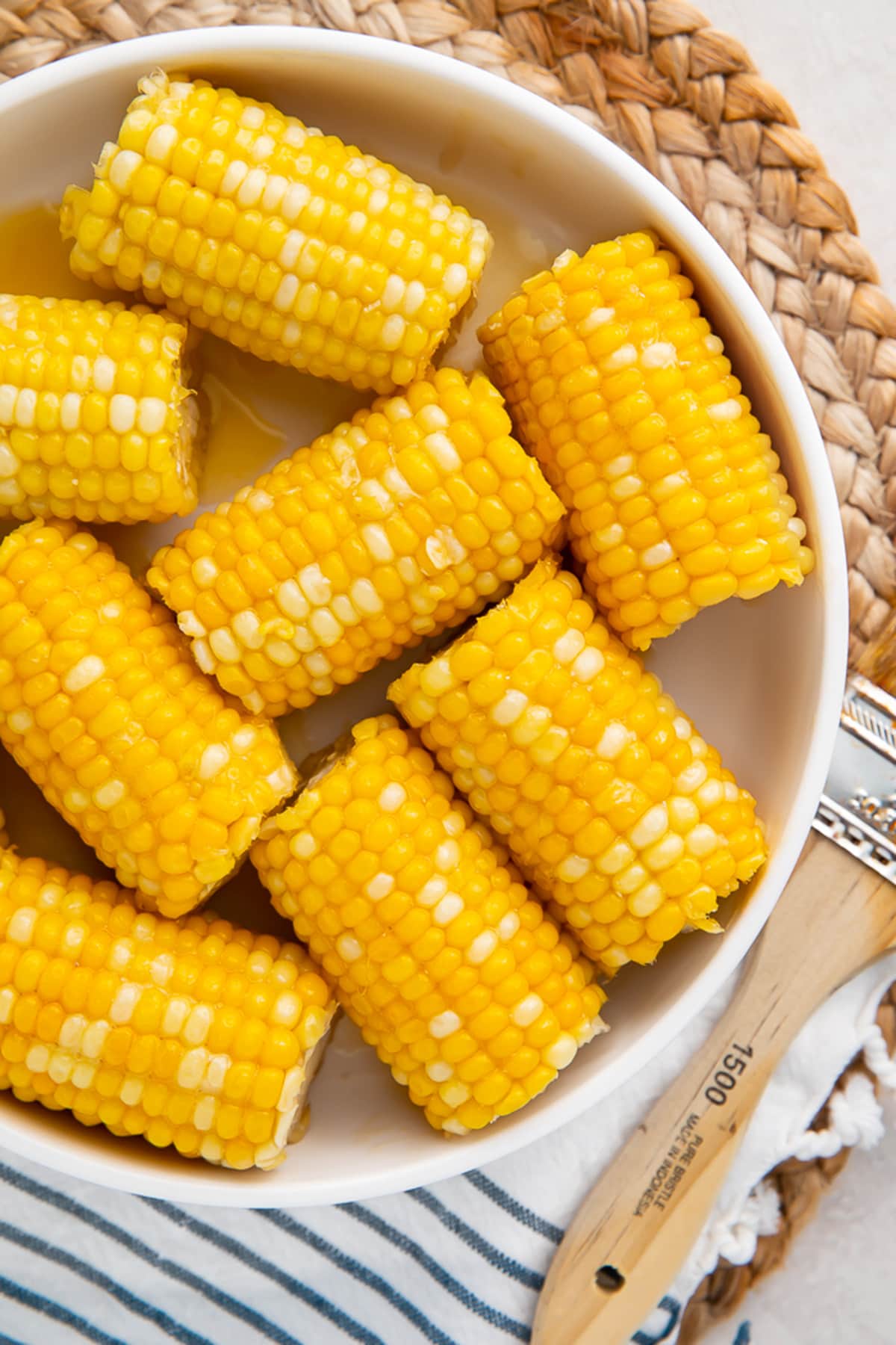 Instant Pot corn on the cob with a honey butter glaze in a large white bowl on a wicker placemat.