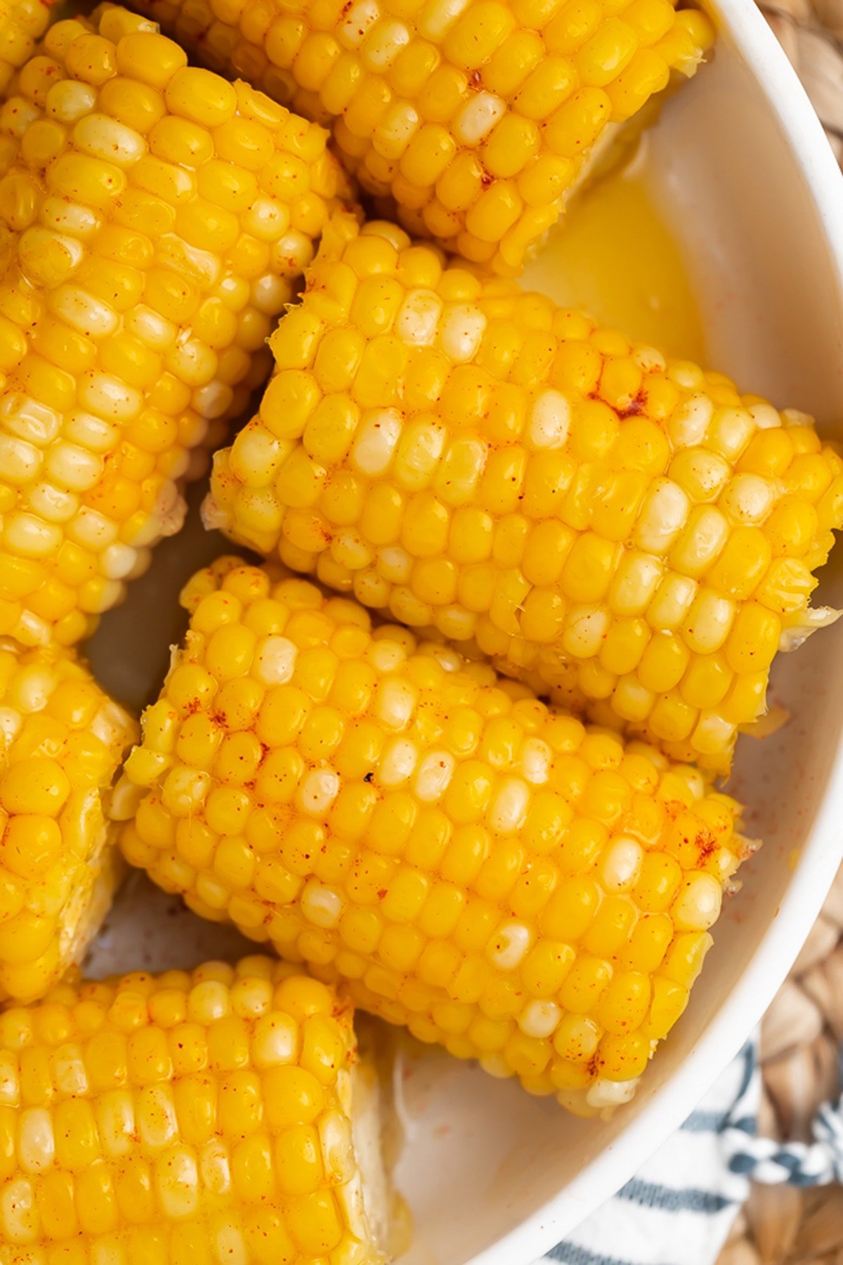 Instant Pot corn on the cob with a honey butter glaze in a large white bowl on a wicker placemat.
