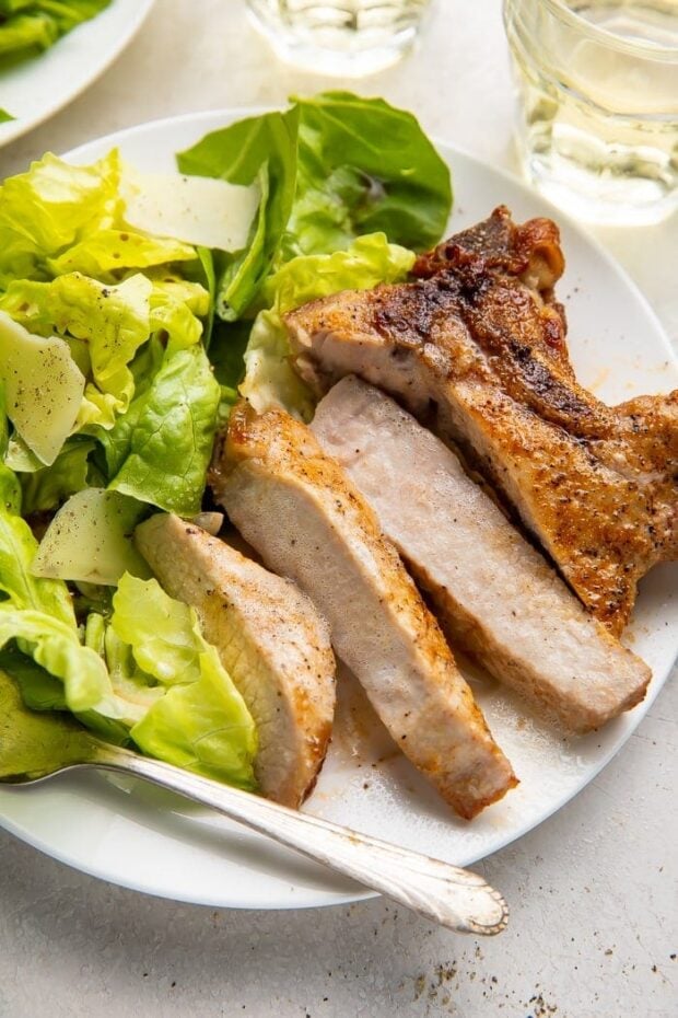 Sliced pork chop cooked in the air fryer with a bed of green veggies on a white plate