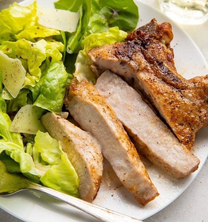 Sliced pork chop cooked in the air fryer with a bed of green veggies on a white plate