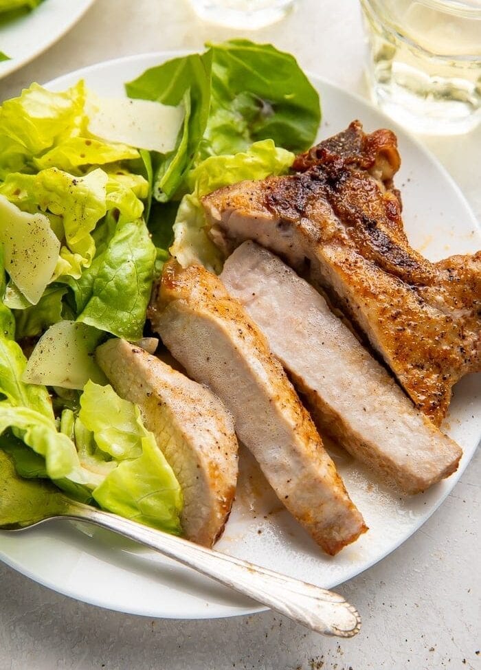 Sliced pork chop cooked in the air fryer with a bed of green veggies on a white plate