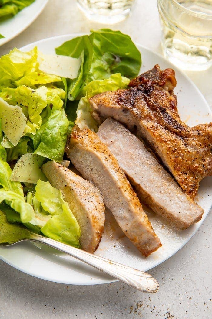 A sliced pork chop on a plate next to some lettuce