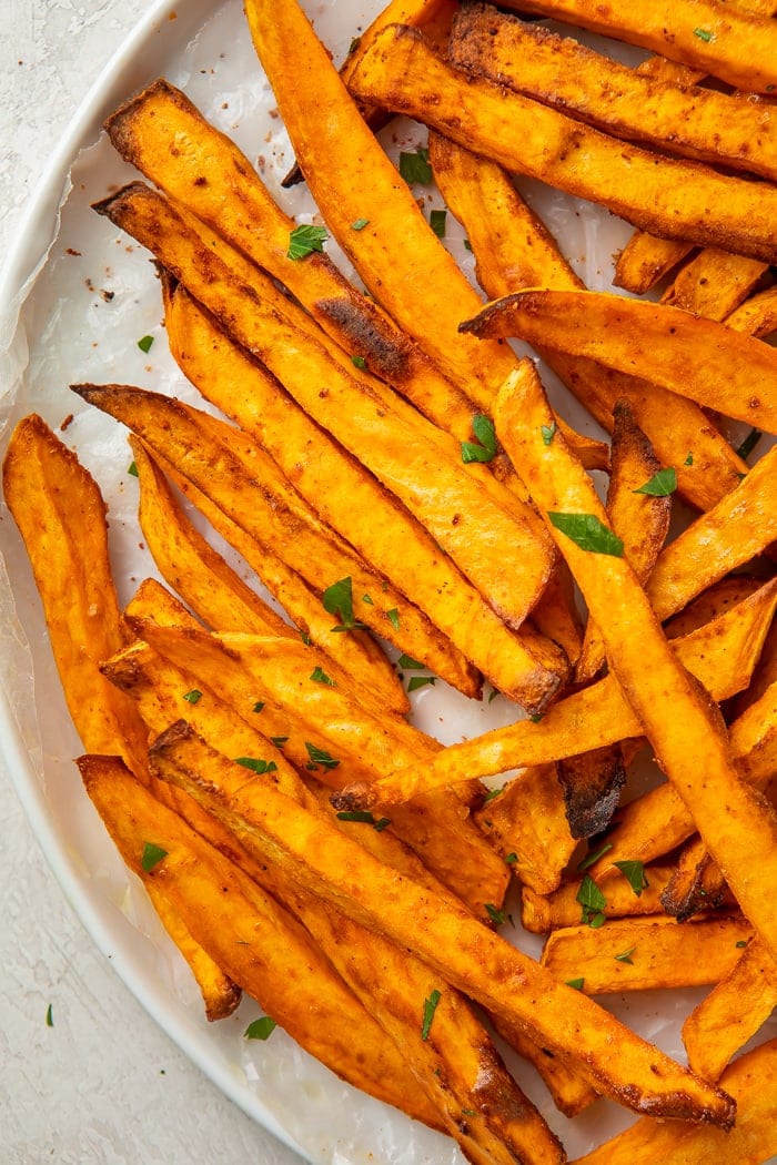 Close-up of sweet potato fries on parchment paper garnished with parsley
