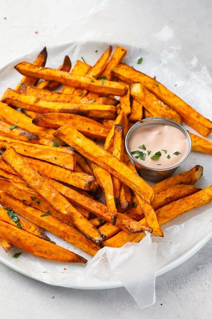 Overhead shot of sweet potato fries on wax paper with dipping sauce