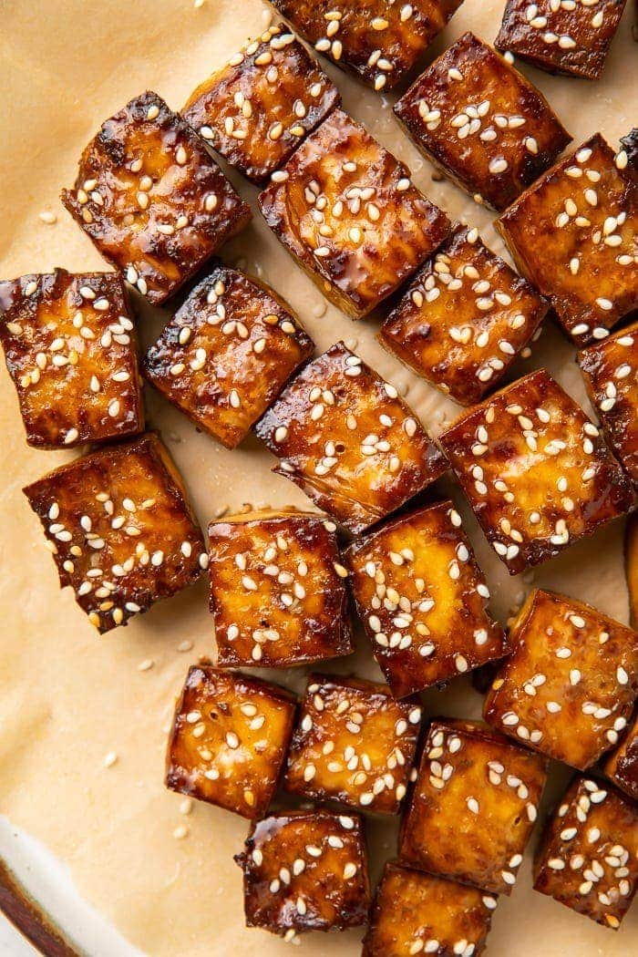 Baked tofu topped with sesame seeds on parchment paper