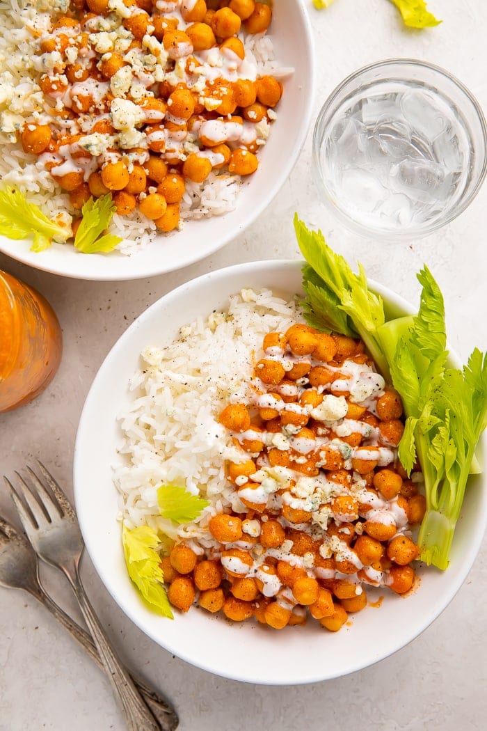 Two bowls of buffalo chickpeas with ranch on a bed of white rice and celery tops