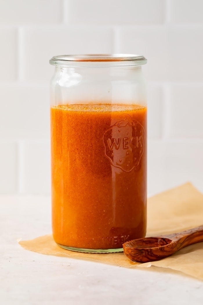 Buffalo sauce in a clear glass jar with a wooden spoon