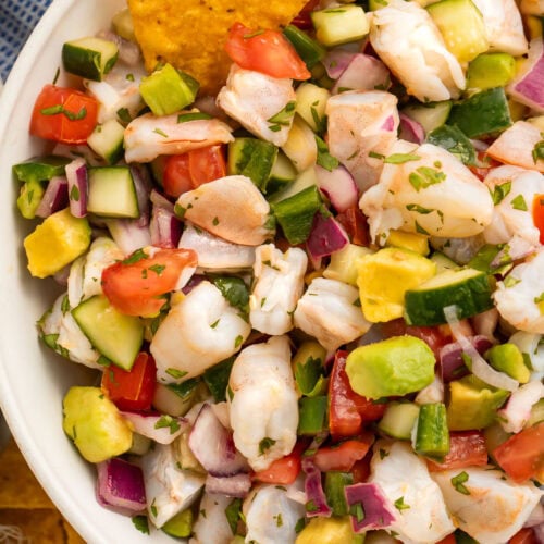 Overhead view of a bowl of easy shrimp ceviche with chunks of shrimp, red onion, cucumber, avocado, and tomatoes.