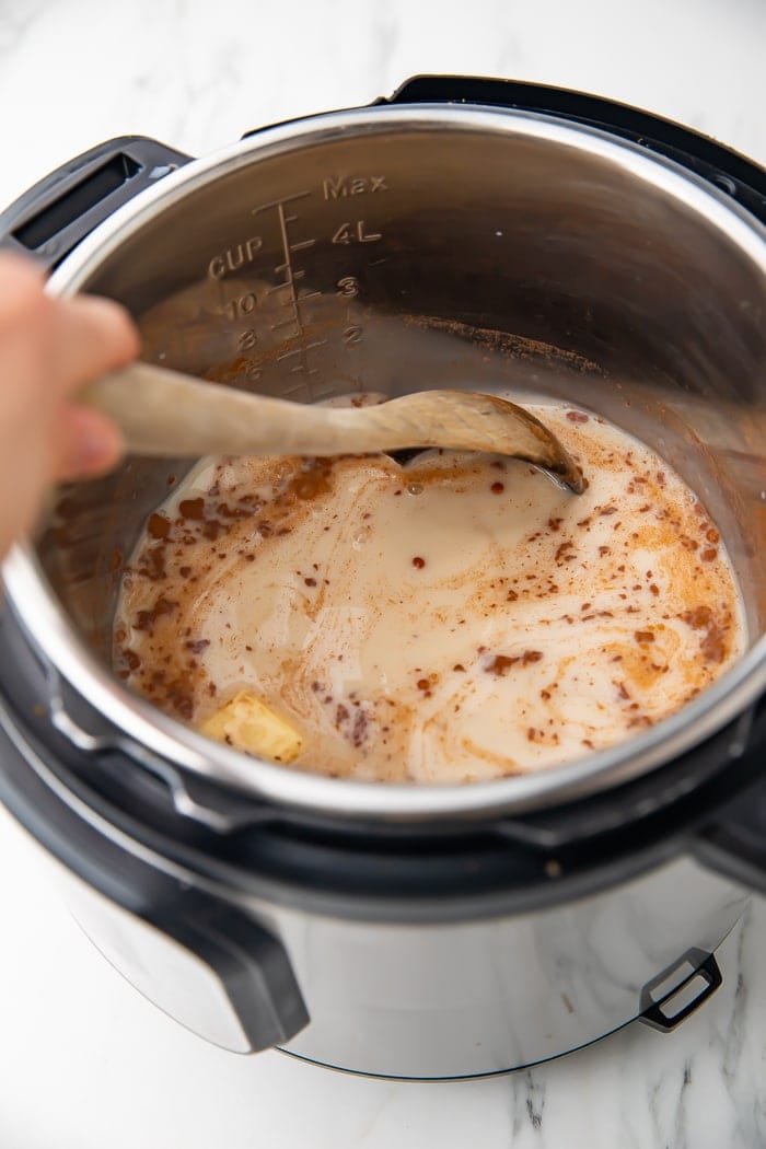 Overhead shot of an Instant Pot with almond milk, rice, and seasonings being stirred