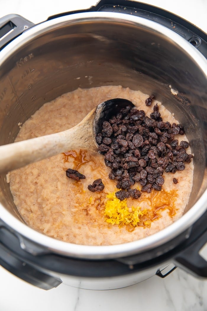 Overhead shot of rice pudding in an Instant Pot with maple syrup, raisins, and lemon zest with a wooden spoon