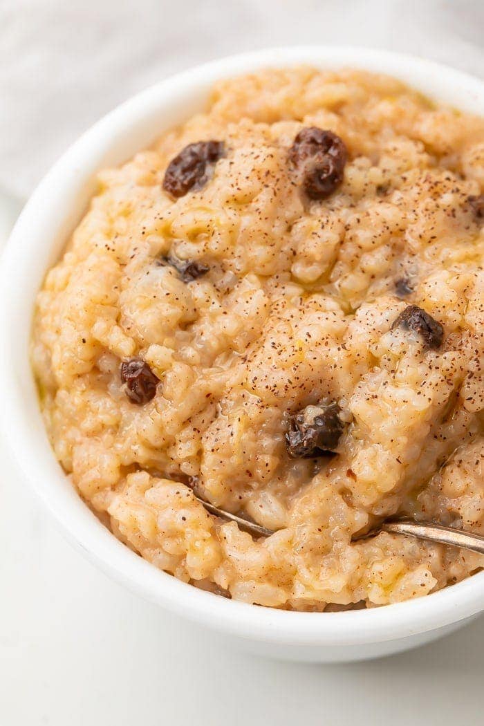 Overhead shot of rice pudding in a white bowl with raisins and sprinkled with cinnamon with a spoon