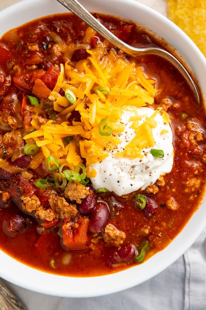 Close-up of turkey chili garnished with shredded cheddar cheese, green onions, and sour cream