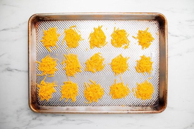 Shredded cheddar cheese piles on baking sheet