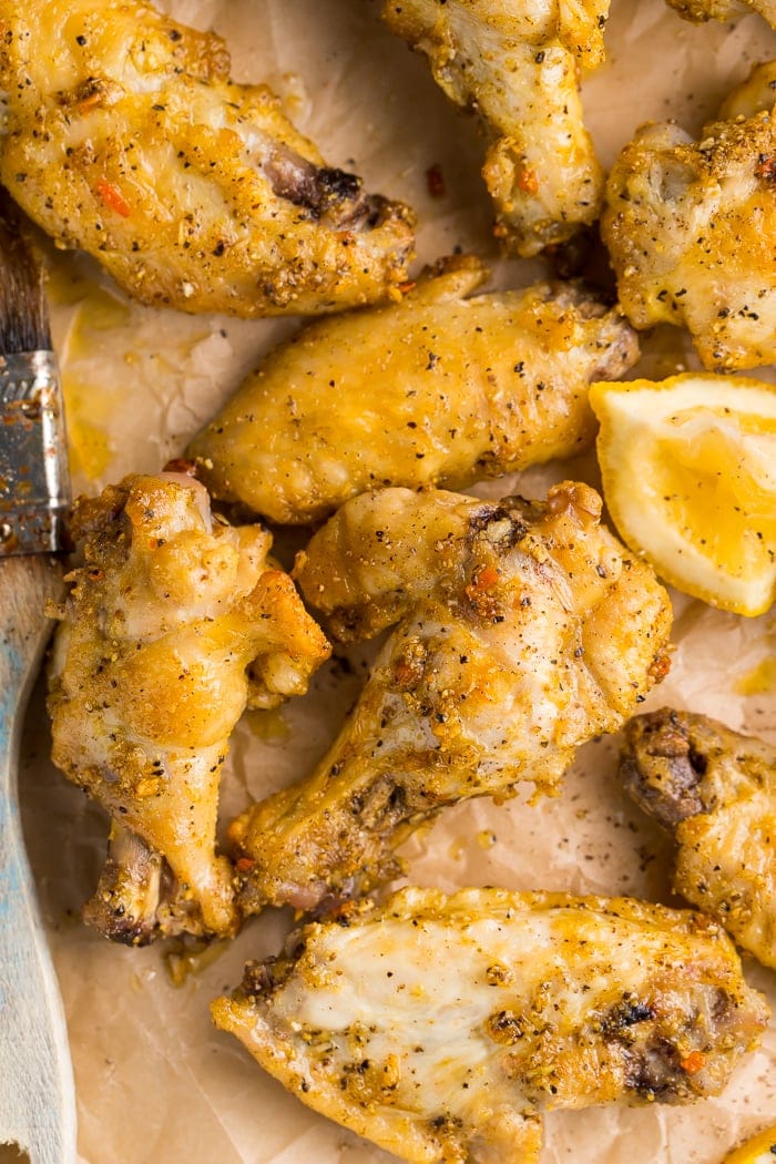 Overhead close-up shot of lemon pepper wings with lemon wedges and a basting brush on parchment paper