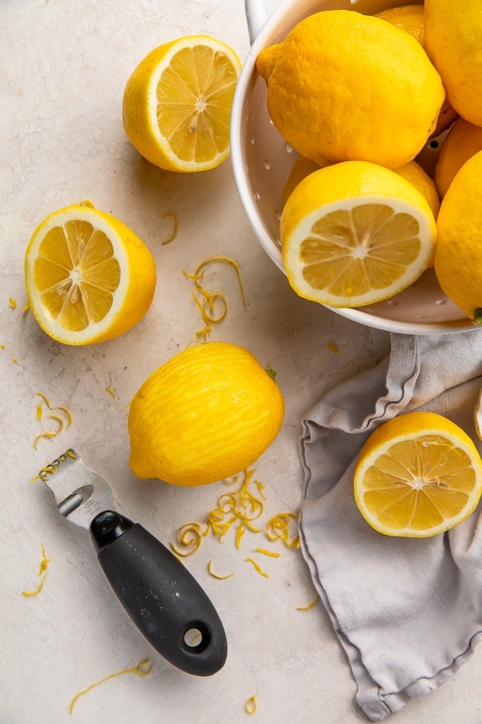 a zested lemon surrounded by lemon zest, a zester, and a colander of lemons