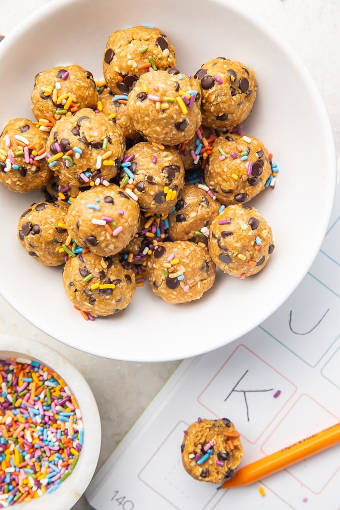 Bowl of peanut butter energy balls with sprinkles next to a child's homework and pencil