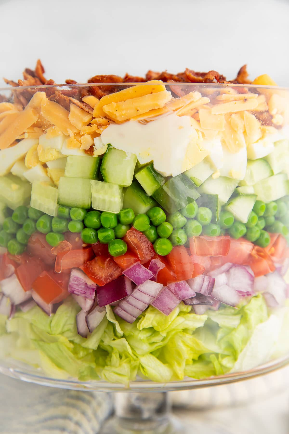 Close-up of a 7 layer salad in a glass trifle dish with a pedestal base.