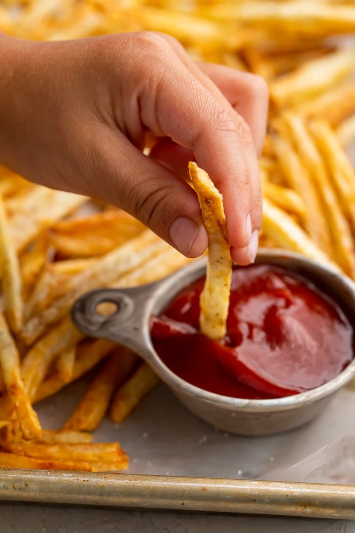 A child's hand dipping a french fry in ketchup
