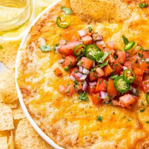 Overhead shot of bean dip in a bowl topped with tomatoes and jalapenos, surrounded by chips and glasses of beer