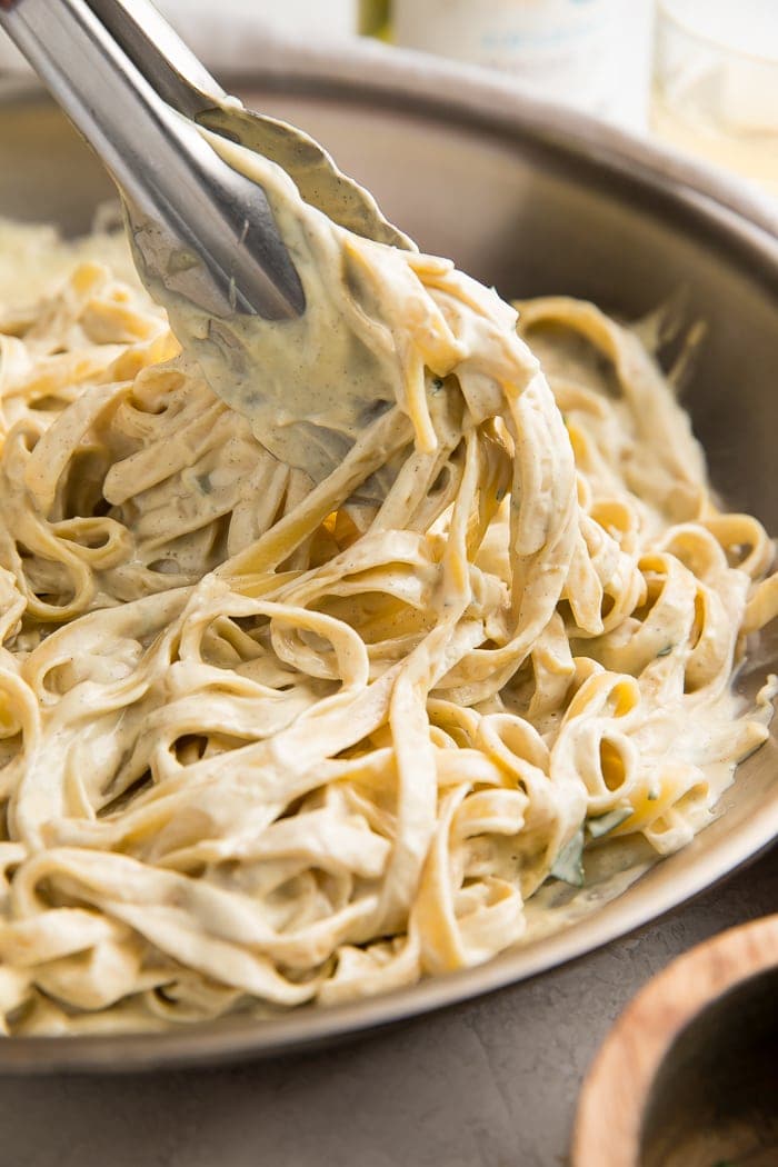 Close up of tongs picking up pasta covered in vegan alfredo sauce