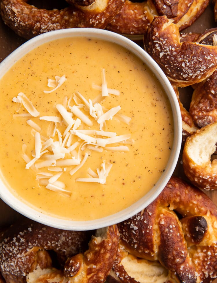 Overhead view of a bowl of beer cheese soup surrounded by salty soft pretzels.