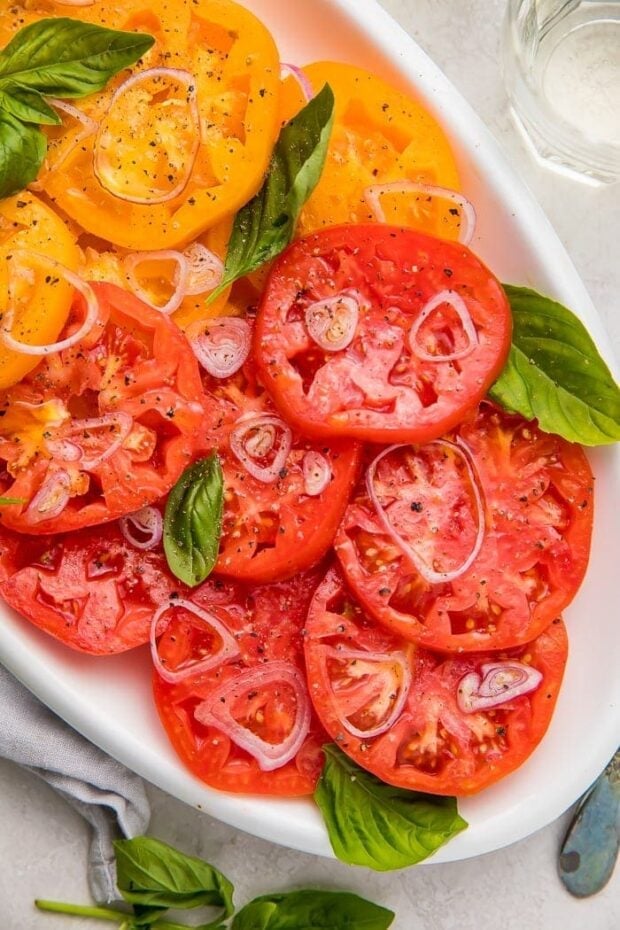 Red and yellow heirloom tomatoes on a serving plate with slices shallots and basil leaves