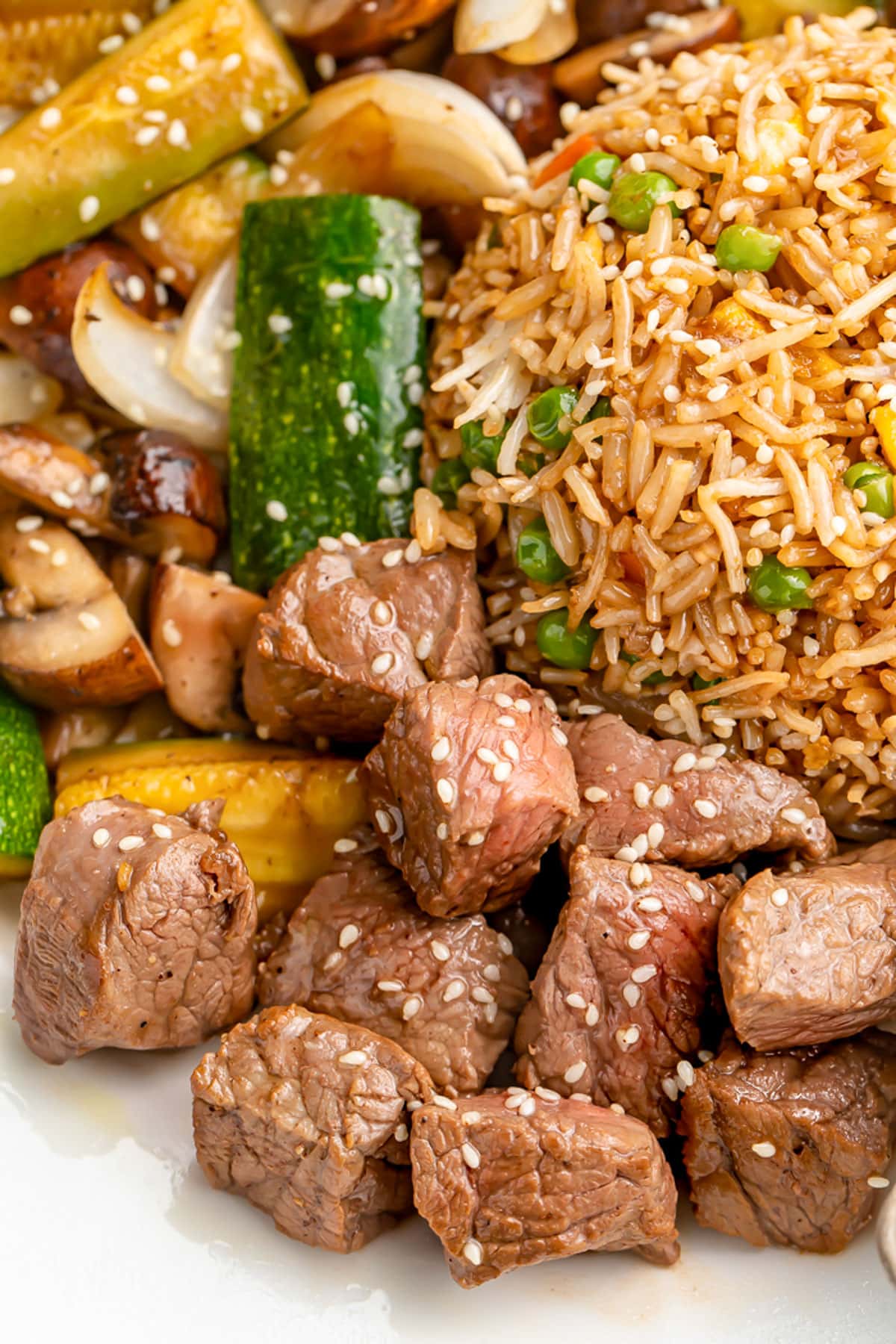 A close-up of hibachi steak garnished with sesame seeds on a plate with fried rice and stir-fry veggies.