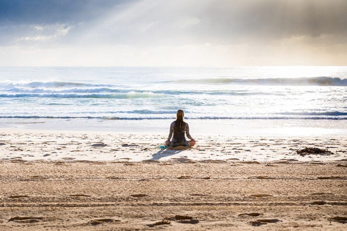 Woman meditating on the beach by the ocean