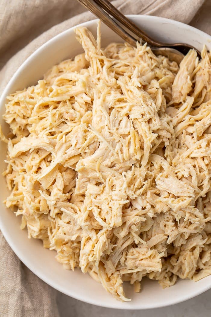 Overhead shot of shredded chicken breasts in a white bowl with two forks