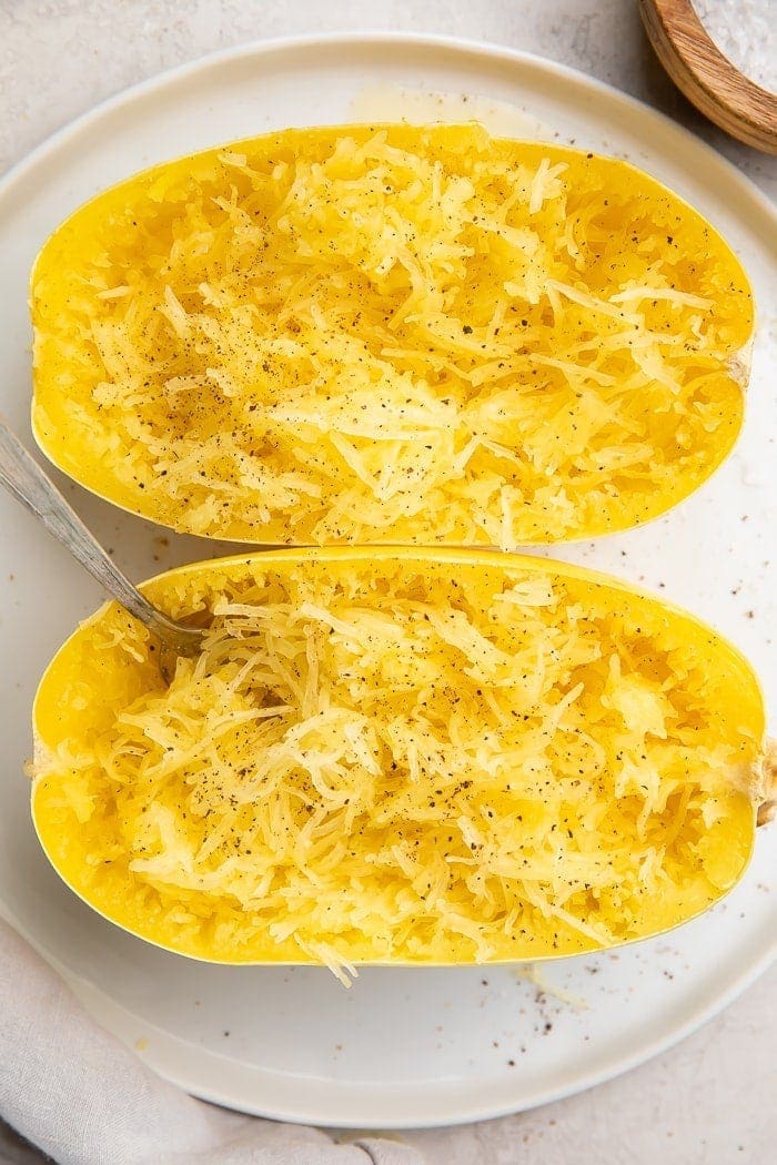 Two halves of a cooked Instant Pot spaghetti squash on a white plate with a fork stuck in one half