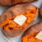 Close up of sweet potatoes cut open and stuffed with butter, salt, and pepper, on a white plate